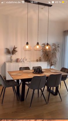 an image of a dining room table and chairs with lights hanging from the ceiling above it