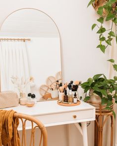 a white desk topped with a mirror next to a potted plant and a wooden chair