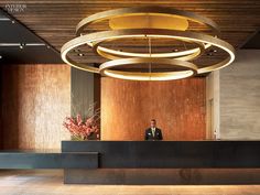 a man sitting at the front desk of a large hotel lobby with circular chandelier