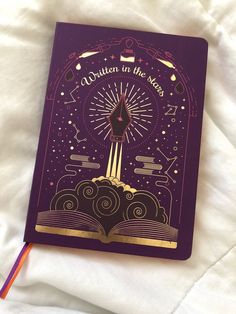 a purple notebook with the words written in gold on it and an open book underneath