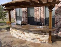 an outdoor kitchen is built into the side of a brick building with a pergolated roof