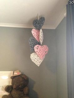 a teddy bear sitting on a bed next to a crocheted heart hanging from the ceiling