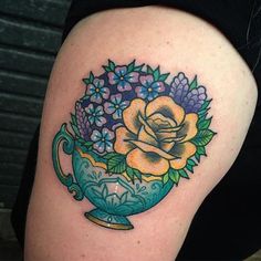 a woman with a tattoo on her arm has a teacup and flowers in it