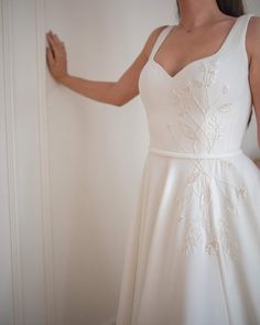 a woman in a white dress is holding her hand out and looking at the wall