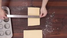 someone using a knife to cut cheese on a wooden table with muffin tins