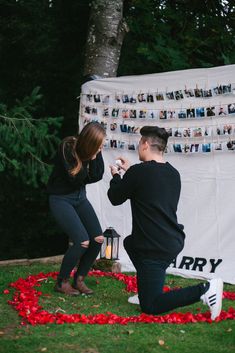 a man kneeling down next to a woman in front of a wall with pictures on it