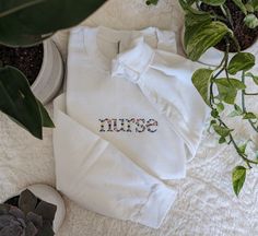 Nurse Floral Sweatshirt This Nurse sweatshirt features a beautiful floral design that adds a touch of femininity to this cozy sweatshirt. It is the perfect gift for the nurse in your life. Comes with a personalized sleeve featuring the nurse's name! Select options from dropdowns for sweatshirt color & size. 1. Name exactly as you want to appear. 2. Thread color for sleeve. (Refer to photos.) Welcome to The Threaded Daisy store. Thank you for visiting!  Production & Shipping: Everything is embroidered to order just for you. On average your items will be shipped out within 3-5 days of ordering. The estimated shipping time in the US is 5-7 business days. Washing Instructions: Wash inside out, in cold water, on gentle cycle.  Tumble dry on low or let air dry. Feedback: If you have any issues w White Custom Embroidered Tops For Loungewear, White Embroidered Sweatshirt For Loungewear, White Embroidered Graphics Sweatshirt For Loungewear, White Sweatshirt With Embroidered Graphics For Loungewear, Cotton Sweater With Floral Embroidery, White Floral Embroidered Sweatshirt For Fall, Casual White Sweatshirt With Floral Embroidery, Embroidered Cotton Sweatshirt For Loungewear, Embroidered Long Sleeve Sweatshirt For Loungewear