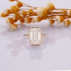 an emerald cut diamond ring sitting next to dried flowers