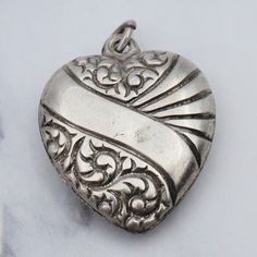 This antique Victorian sterling charm features a puffy heart design adorned with ornate engraved motifs and a blank banner running diagonally across the heart; the design is the same on both sides. This pendant weighs 1.1 grams and measures 18mm tall, not including the jump ring. It is in good antique condition with some wear, there are some visible dings. Item is marked as shown; some of the marking has worn off.  *I have many styles of necklace chains available Antique Silver Engraved Heart Jewelry, Victorian Silver Jewelry For Valentine's Day, Antique Silver Engraved Jewelry For Valentine's Day, Engraved Antique Silver Jewelry For Valentine's Day, Valentine's Day Vintage Etched Jewelry, Victorian Engraved Heart Jewelry, Vintage Etched Heart Pendant Jewelry, Antique Heart-shaped Silver Jewelry, Antique Etched Heart Jewelry