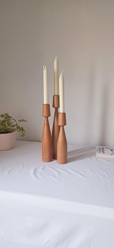 three wooden candlesticks sitting on top of a white table next to a potted plant