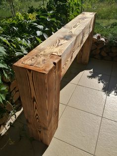 a wooden bench sitting on top of a tiled floor next to bushes and trees in the background