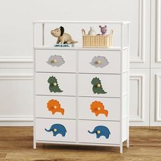 an animal themed dresser in a room with white walls and wooden floors, including a toy elephant sitting on top of the drawers