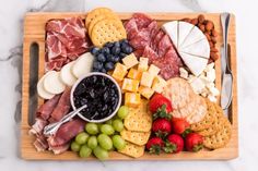 a wooden platter filled with cheese, crackers, fruit and meats on a marble counter top