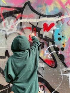 a person in a green hoodie painting graffiti on a wall