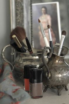 a silver vase filled with makeup brushes on top of a table next to a mirror