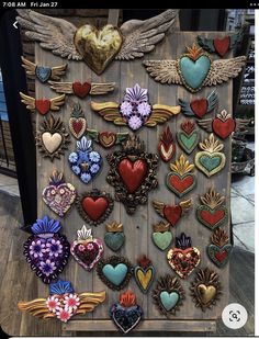 an assortment of heart shaped brooches are displayed on a wooden board with angel wings