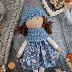 a doll with brown hair wearing a blue dress and knitted hat on a wooden surface