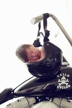 a baby is sleeping on top of a motorcycle helmet hanging from the handlebars