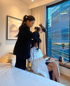 a woman is getting her hair done in front of a window with a city view