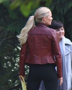 a woman in black pants and a red leather jacket is walking with another woman behind her