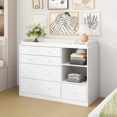 a white dresser with drawers and pictures on the wall