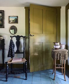 a chair and table in a room with wooden floors, green doors and pictures on the wall