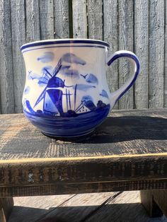 a blue and white coffee cup sitting on top of a wooden table next to a fence