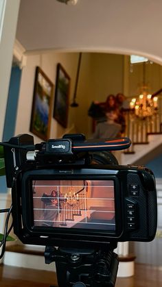 a video camera sitting on top of a wooden table in front of a staircase and chandelier