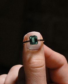 a woman's hand holding a ring with an emerald stone