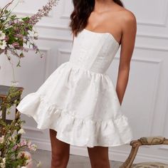 a woman standing in front of a chair wearing a white dress