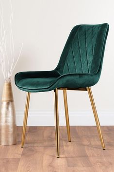 a green velvet chair next to a gold vase