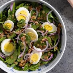 a salad with hard boiled eggs, onions and spinach in a blue and white bowl