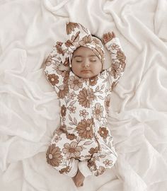 a baby is laying down on a white blanket and wearing a brown floral outfit with an attached headband