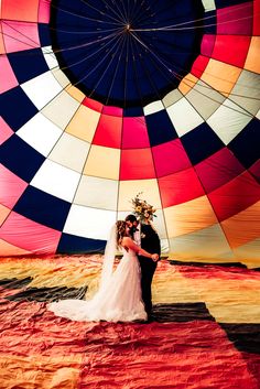 a bride and groom standing in front of a colorful hot air balloon at their wedding