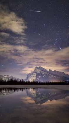 the night sky with stars above mountains and trees reflected in a still body of water