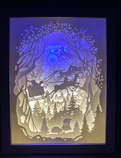 an illuminated paper cut depicting santa riding his sleigh through the woods with reindeers