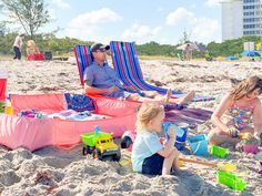 two adults and one child sitting on the beach with toys in front of them,