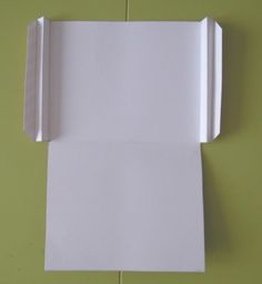 a piece of white paper is folded up on a green surface with the corner cut out