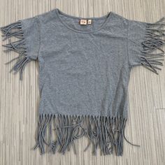 a gray shirt with fringes on it laying on the floor in front of a wall