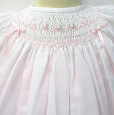 a white dress with pink trimmings and flowers on the collarline is shown