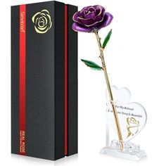 a purple rose in a glass vase next to a black box