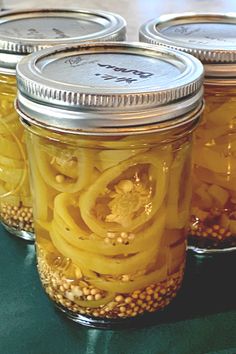 four jars filled with pickled onions on top of a green tablecloth covered counter