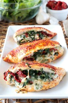 two pieces of chicken with spinach and cheese on a white plate next to a bowl of strawberries