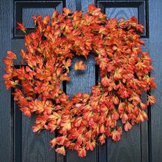 a wreath is hanging on the front door with red and orange flowers in it's center