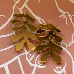 two pairs of gold toned earrings on a pink and white patterned tablecloth with leaves