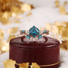 a blue stone ring sitting on top of a wooden box with gold leaves around it