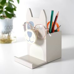 a pen holder with glasses and pencils in it on a white table next to a potted plant