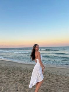 a woman in a white dress is walking on the sand at the beach near the ocean