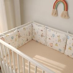 a crib bed with a rainbow wall hanging on the wall and pillows in front of it