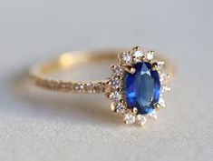 an oval shaped blue sapphire and diamond ring on a white surface with the top half partially covered in gold